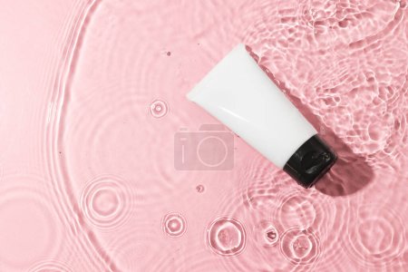 Téléchargez les photos : Tube de produit de beauté dans l'eau avec fond d'espace de copie sur fond rose. Santé et beauté, concept maquillage et beauté. - en image libre de droit