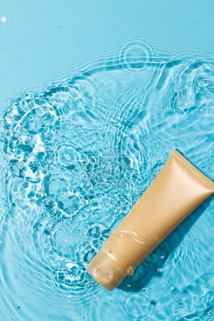 Photo for Vertical image of beauty product tube in water with copy space background on blue background. Health and beauty, make up and beauty concept. - Royalty Free Image