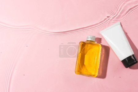 Téléchargez les photos : Bouteille de produit de beauté et tube dans l'eau avec fond d'espace de copie sur fond rose. Santé et beauté, concept maquillage et beauté. - en image libre de droit