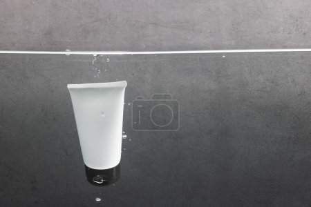 Photo for Beauty product tube falling into water with copy space background on grey background. Health and beauty, make up and beauty concept. - Royalty Free Image