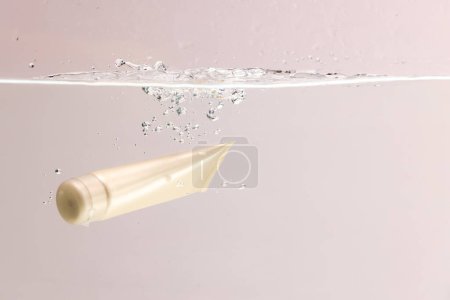 Photo for Beauty product tube falling into water with copy space background on pink background. Health and beauty, make up and beauty concept. - Royalty Free Image