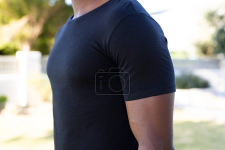 Photo for Mid section of african american man in black t-shirt with copy space in garden. Clothes, fashion and casual clothes concept, unaltered. - Royalty Free Image