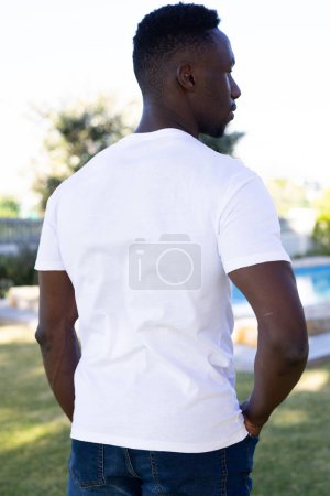 Photo for Vertical image of rear view of african american man in white t-shirt with copy space in garden. Clothes, fashion and casual clothes concept, unaltered. - Royalty Free Image