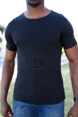 Téléchargez les photos : Image verticale de la section médiane de l'homme afro-américain en t-shirt noir avec espace de copie dans le jardin. Vêtements, concept de mode et de vêtements décontractés, inchangés. - en image libre de droit