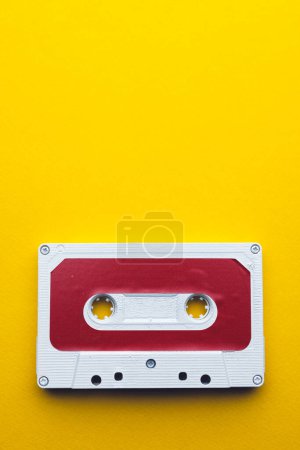 Photo for Overhead view of red and white cassette tape with copy space on yellow background. Music, sound, listening, entertainment and nostalgia concept. - Royalty Free Image