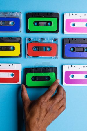 Téléchargez les photos : Vue aérienne de la main afro-américaine avec cassettes colorées disposées sur fond bleu. Concept de musique, son, écoute, divertissement et nostalgie. - en image libre de droit