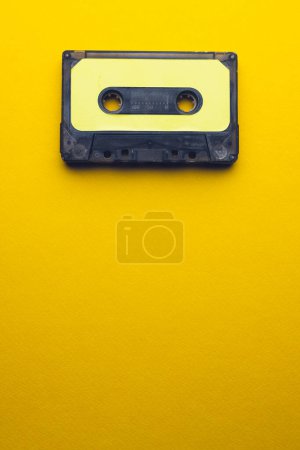 Photo for Overhead view of black and yellow cassette tape with copy space on yellow background. Music, sound, listening, entertainment and nostalgia concept. - Royalty Free Image