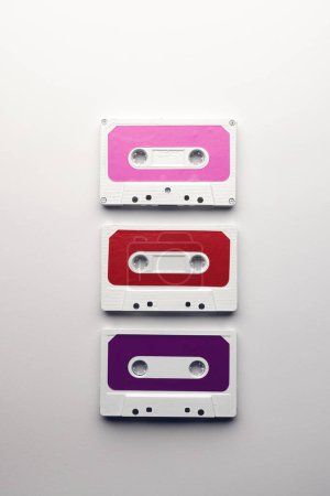 Téléchargez les photos : Vue aérienne de trois cassettes colorées disposées sur fond blanc. Concept de musique, son, écoute, divertissement et nostalgie. - en image libre de droit