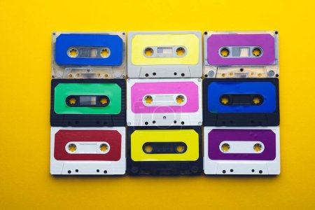 Foto de Vista aérea de nueve cintas de cassette coloridas dispuestas sobre fondo amarillo. Música, sonido, escucha, entretenimiento y concepto de nostalgia. - Imagen libre de derechos