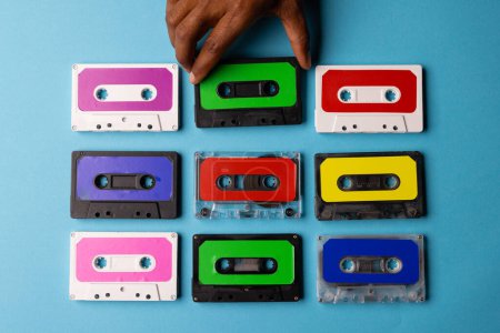 Téléchargez les photos : Vue aérienne de la main afro-américaine avec cassettes colorées disposées sur fond bleu. Concept de musique, son, écoute, divertissement et nostalgie. - en image libre de droit