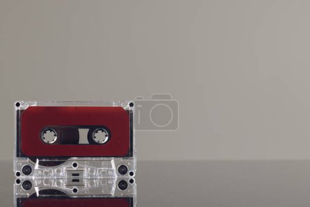 Téléchargez les photos : Gros plan de cassette rouge sur fond gris avec réflexion. Concept de musique, son, écoute, divertissement et nostalgie. - en image libre de droit