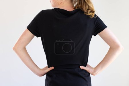 Téléchargez les photos : Vue arrière de la femme caucasienne en t-shirt noir et espace de copie sur fond blanc. Vêtements, concept de mode et de vêtements décontractés, inchangés. - en image libre de droit