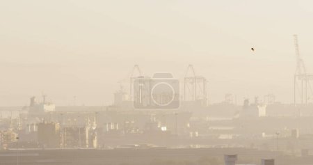 Foto de Una vista borrosa de un puerto con grúas y barcos, con espacio para copias. La imagen captura la atmósfera industrial de una zona ocupada durante una mañana brumosa. - Imagen libre de derechos