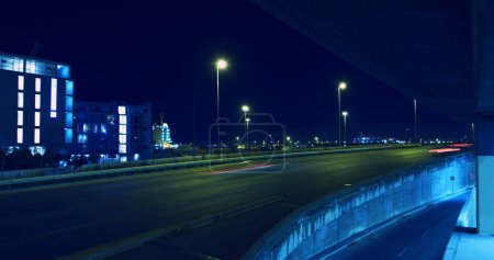 Foto de Una autopista de la ciudad por la noche iluminada por farolas. Larga exposición captura los senderos de luz de los vehículos en movimiento, haciendo hincapié en la actividad nocturna de la ciudad. - Imagen libre de derechos
