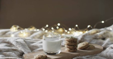 Téléchargez les photos : Un verre de lait et des biscuits sur un lit confortable, avec espace de copie. Les lumières chaudes ajoutent une ambiance réconfortante à ce cadre familial, parfait pour une collation relaxante. - en image libre de droit