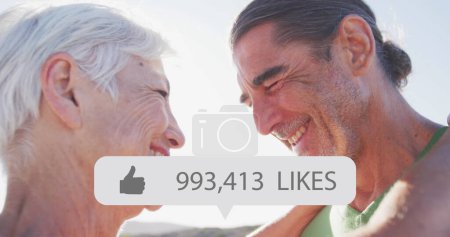 Foto de Imagen de la burbuja del habla con el pulgar hacia arriba icono y números sobre feliz pareja de ancianos en la playa. interfaz digital, redes sociales y concepto de red global imagen generada digitalmente. - Imagen libre de derechos