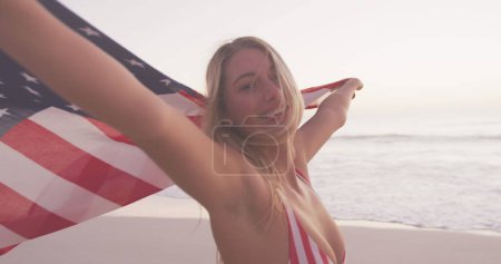 Foto de Imagen del texto del día de la independencia sobre una mujer sonriente envuelta en bandera americana en la playa. usa patriotismo y democracia concepto de imagen generada digitalmente. - Imagen libre de derechos