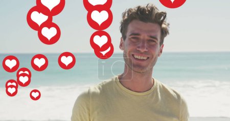 Téléchargez les photos : Image des icônes du cœur des médias sociaux sur le portrait d'un homme souriant sur la plage. interface numérique, médias sociaux et concept de réseau mondial image générée numériquement. - en image libre de droit