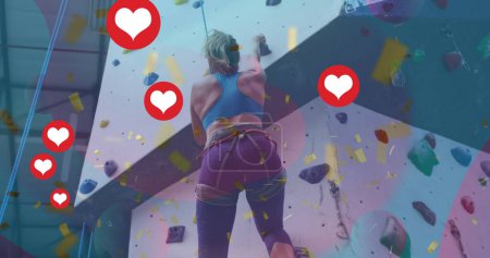 Mehrere Herzsymbole schweben gegen die kaukasisch fitte Frau, die in der Turnhalle an der Wand klettert. Sport-, Fitness- und Social-Media-Netzwerktechnologiekonzept