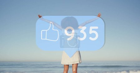 Téléchargez les photos : Image de bulle de parole avec les pouces vers le haut icône et numéros sur la femme avec les bras tendus sur la plage. interface numérique, médias sociaux et concept de réseau mondial image générée numériquement. - en image libre de droit