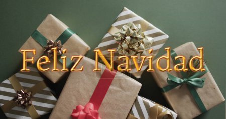 Photo for Feliz navidad text in orange over christmas gifts on green background. Christmas, tradition, greetings and celebration digitally generated image. - Royalty Free Image