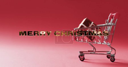 Téléchargez les photos : Un panier miniature contient un cadeau, symbolisant les achats de vacances. La toile de fond festive avec le texte "Joyeux Noël" suggère la saison du don et de l'excitation au détail. - en image libre de droit