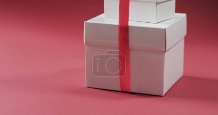 Foto de Cajas de regalo blancas con cinta roja sobre fondo rosa. Los regalos se asocian a menudo con celebraciones como cumpleaños o días festivos. - Imagen libre de derechos