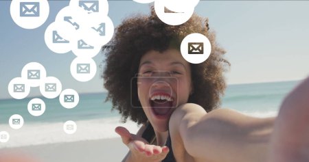 Foto de Imagen de los iconos de correo electrónico de las redes sociales sobre la mujer sonriente sonriendo a la cámara en la playa. interfaz digital, redes sociales y concepto de red global imagen generada digitalmente. - Imagen libre de derechos