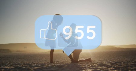 Foto de Like icon and increasing numbers against man proposing his girlfriends with a ring on the beach. social media networking and love relationship concept - Imagen libre de derechos