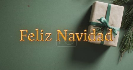Photo for Feliz navidad text in orange over christmas gift on green background. Christmas, tradition, greetings and celebration digitally generated image. - Royalty Free Image