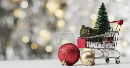 Foto de Un carrito de compras en miniatura contiene decoraciones navideñas. Los adornos festivos simbolizan las compras de temporada y la celebración. - Imagen libre de derechos