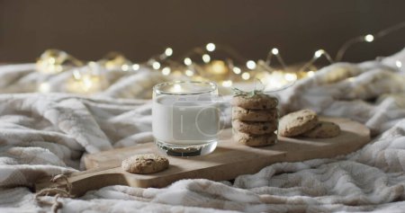 Foto de Un vaso de leche y galletas sobre una manta acogedora, con espacio para copiar. Las luces cálidas agregan un ambiente hogareño, lo que sugiere un ambiente cómodo en el hogar para un aperitivo.. - Imagen libre de derechos