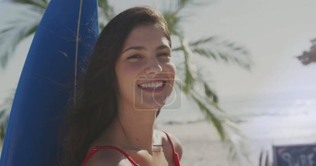 Téléchargez les photos : Jeune femme caucasienne bénéficie d'une journée de plage ensoleillée, avec espace de copie. Elle respire le bonheur avec une planche de surf, soulignant un style de vie en plein air détendu. - en image libre de droit