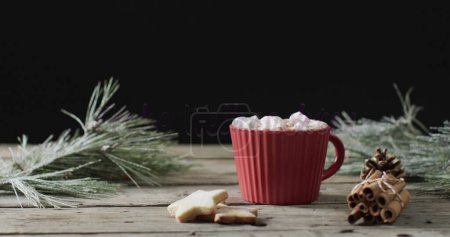 Foto de Una taza de chocolate caliente acogedor rodeado de decoración festiva. Las ramas de pino y los palitos de canela añaden un toque navideño a la mesa de madera rústica. - Imagen libre de derechos