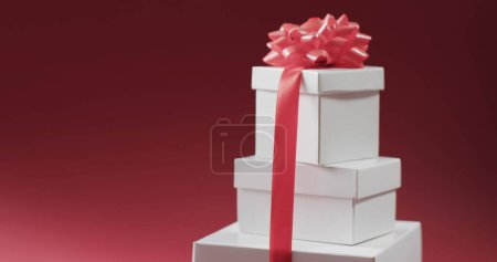 Tres cajas de regalo apiladas atadas con una cinta rosa, colocadas sobre un fondo rojo. Regalos como estos a menudo se asocian con celebraciones como cumpleaños, días festivos o aniversarios.