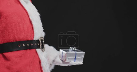 Photo for Santa Claus holds a small gift, with copy space. The image captures the essence of holiday giving and festive cheer. - Royalty Free Image