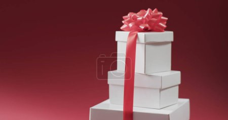Foto de Cajas de regalo blancas apiladas con una cinta rosa sobre un fondo rojo. El arreglo sugiere una ocasión especial o una celebración festiva. - Imagen libre de derechos