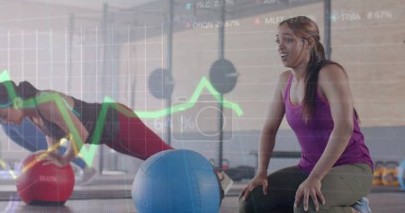 Foto de Imagen de datos sobre gráficos sobre diversas mujeres que cruzan el entrenamiento con bolas de medicina en el gimnasio. Fitness, ejercicio, fuerza, datos, interfaz digital y tecnología de imagen generada digitalmente. - Imagen libre de derechos