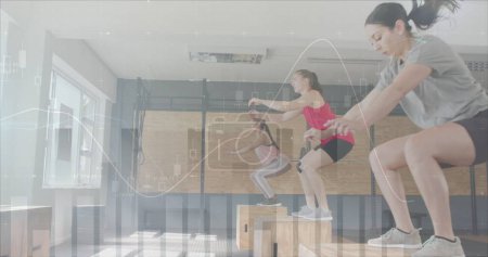 Foto de Imagen del procesamiento de datos en gráfico sobre diversas mujeres que saltan en cajas de entrenamiento cruzado en el gimnasio. Fitness, ejercicio, fuerza, datos, interfaz digital y tecnología de imagen generada digitalmente. - Imagen libre de derechos