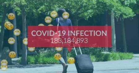 Photo for Image of covid 19 infection numbers end emojis over woman with suitcase wearing face mask. global covid 19 pandemic, health and medicine concept digitally generated image. - Royalty Free Image