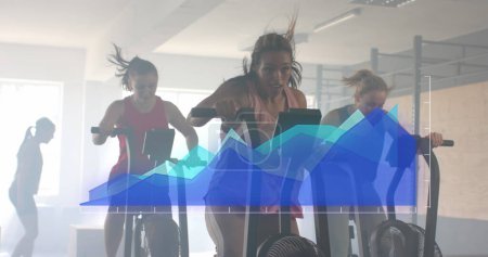 Foto de Imagen del procesamiento de datos en gráfico azul sobre diversas mujeres que cruzan el entrenamiento en elípticas en el gimnasio. Fitness, ejercicio, fuerza, datos, interfaz digital y tecnología de imagen generada digitalmente. - Imagen libre de derechos
