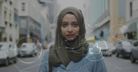 Photo for Image of connected media icons with smiling woman wearing hijab walking in street. communication technology digital interface concept, digitally generated image. media - Royalty Free Image