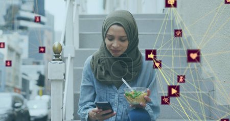 Téléchargez les photos : Image d'un réseau d'icônes des médias connectés avec une femme portant du hijab mangeant dans la rue. technologie de communication concept d'interface numérique, image générée numériquement. - en image libre de droit