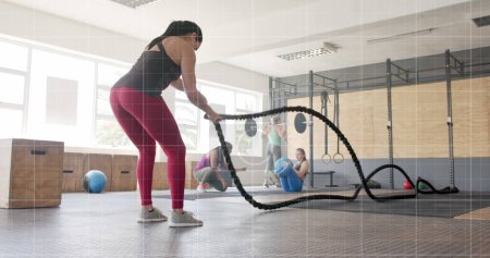 Photo for Image of graph processing data over caucasian woman cross training with battle ropes at gym. Fitness, exercise, strength, data, digital interface and technology digitally generated image. - Royalty Free Image