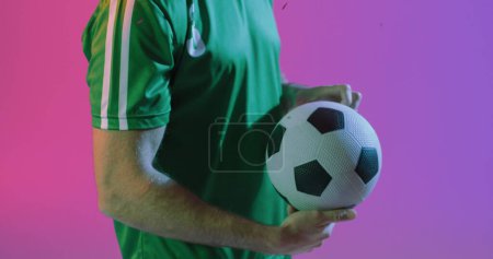 Bild des kaukasischen männlichen Fußballers hält Ball. Globaler Sport und digitales Schnittstellenkonzept digital generiertes Image.
