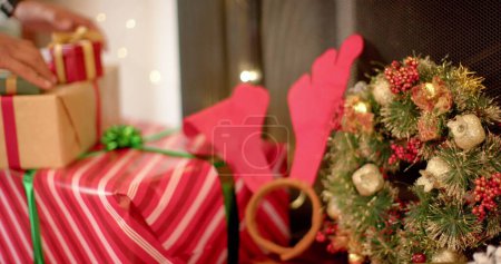 Téléchargez les photos : Mains d'une personne enveloppant des cadeaux pour la saison des fêtes à la maison. Papier d'emballage coloré et décorations évoquent la chaleur des traditions de vacances. - en image libre de droit