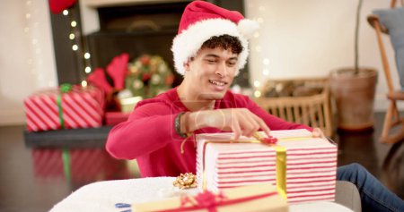 Photo for Young biracial man wrapping gifts at home, with copy space. He's preparing presents with festive decorations around him. - Royalty Free Image