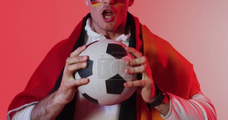 Junger Mann aus dem Kaukasus posiert als Superheld mit einem Fußball. Sein Kostüm suggeriert eine spielerische Sicht auf Sport und Heldentum bei einer Themenveranstaltung oder Party.