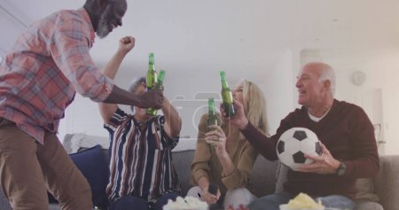Photo for Diverse group celebrates a goal at home, with copy space. Friends share a toast with beers during a soccer match viewing party. - Royalty Free Image