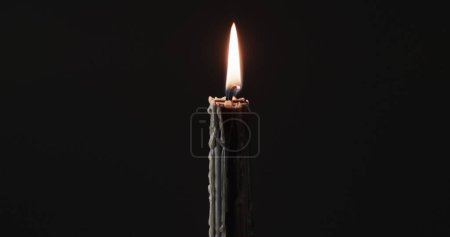 Image of merry christmas text over lit candle on black background. Christmas, tradition and celebration concept digitally generated image.